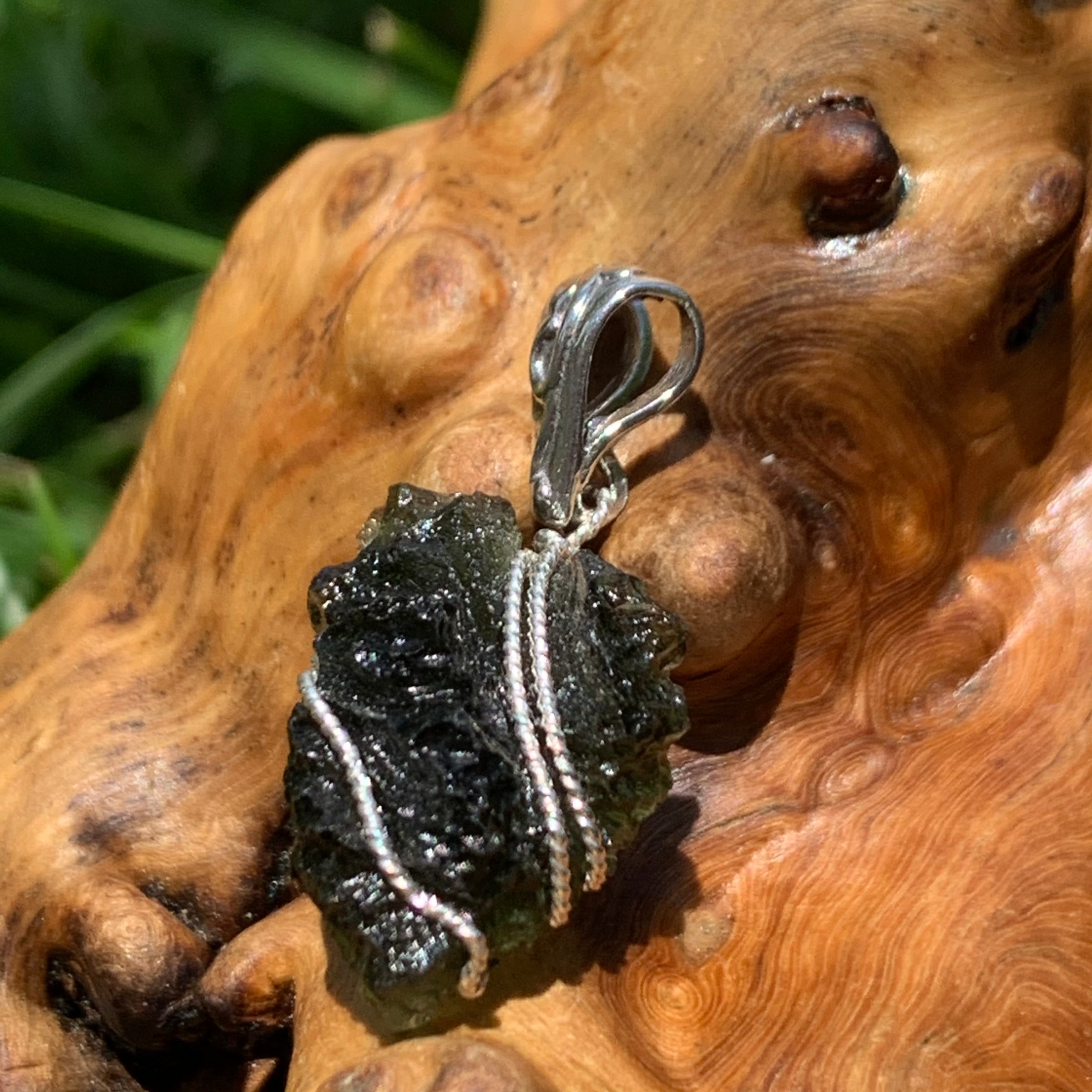 Moldavite pendant wire wrapped in sterling silver sitting on driftwood for display