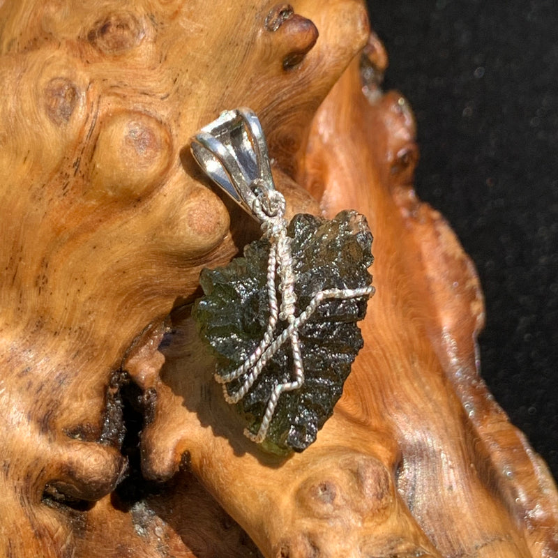 back view of moldavite pendant wire wrapped in sterling silver sitting on driftwood for display