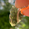 Moldavite pendant wire wrapped in sterling silver held in a hand with light shining through