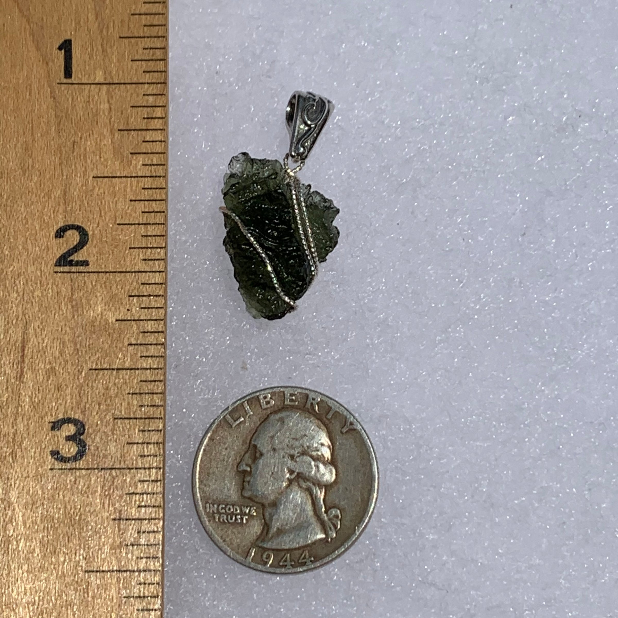 Wire wrapped moldavite pendant next to a ruler and US quarter to show scale