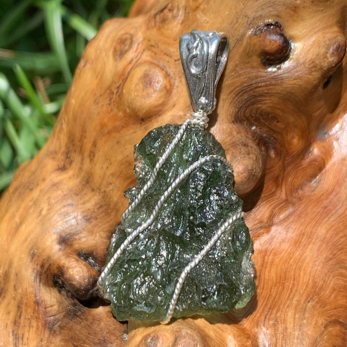 Moldavite pendant wire wrapped in sterling silver sitting on driftwood for display