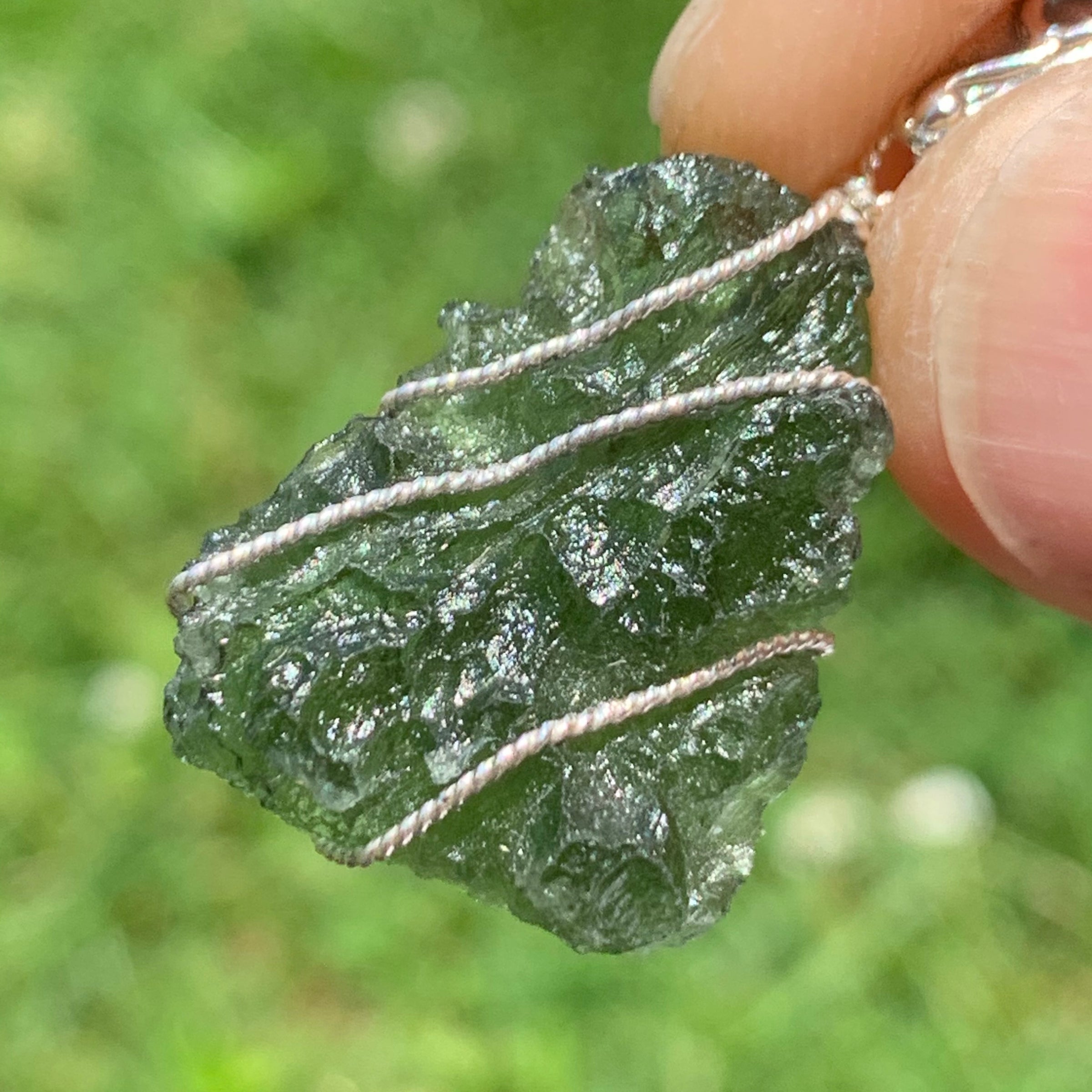 Moldavite pendant wire wrapped in sterling silver held in a hand with light shining through