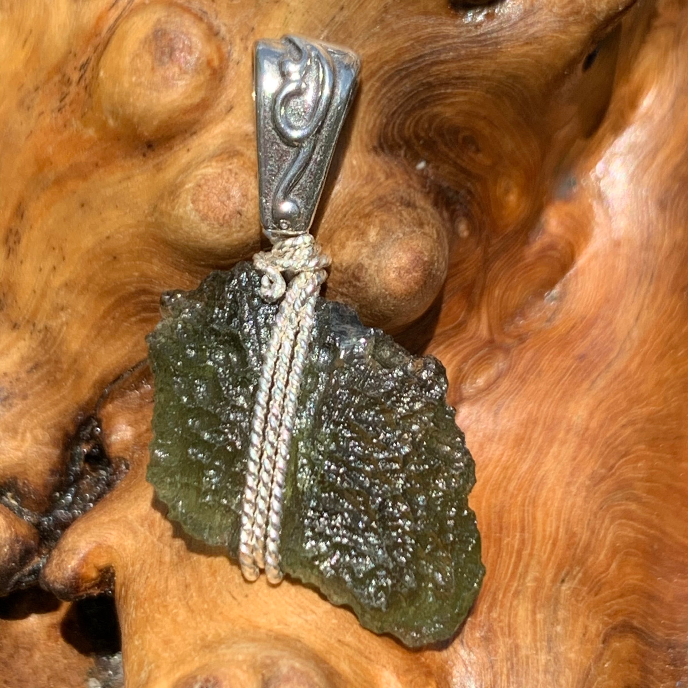 Moldavite pendant wire wrapped in sterling silver sitting on driftwood for display