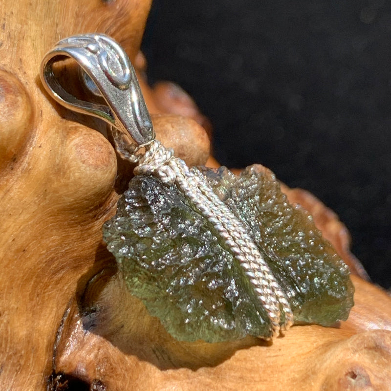 Moldavite pendant wire wrapped in sterling silver sitting on driftwood for display