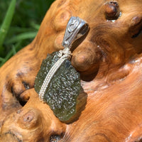 Moldavite pendant wire wrapped in sterling silver sitting on driftwood for display