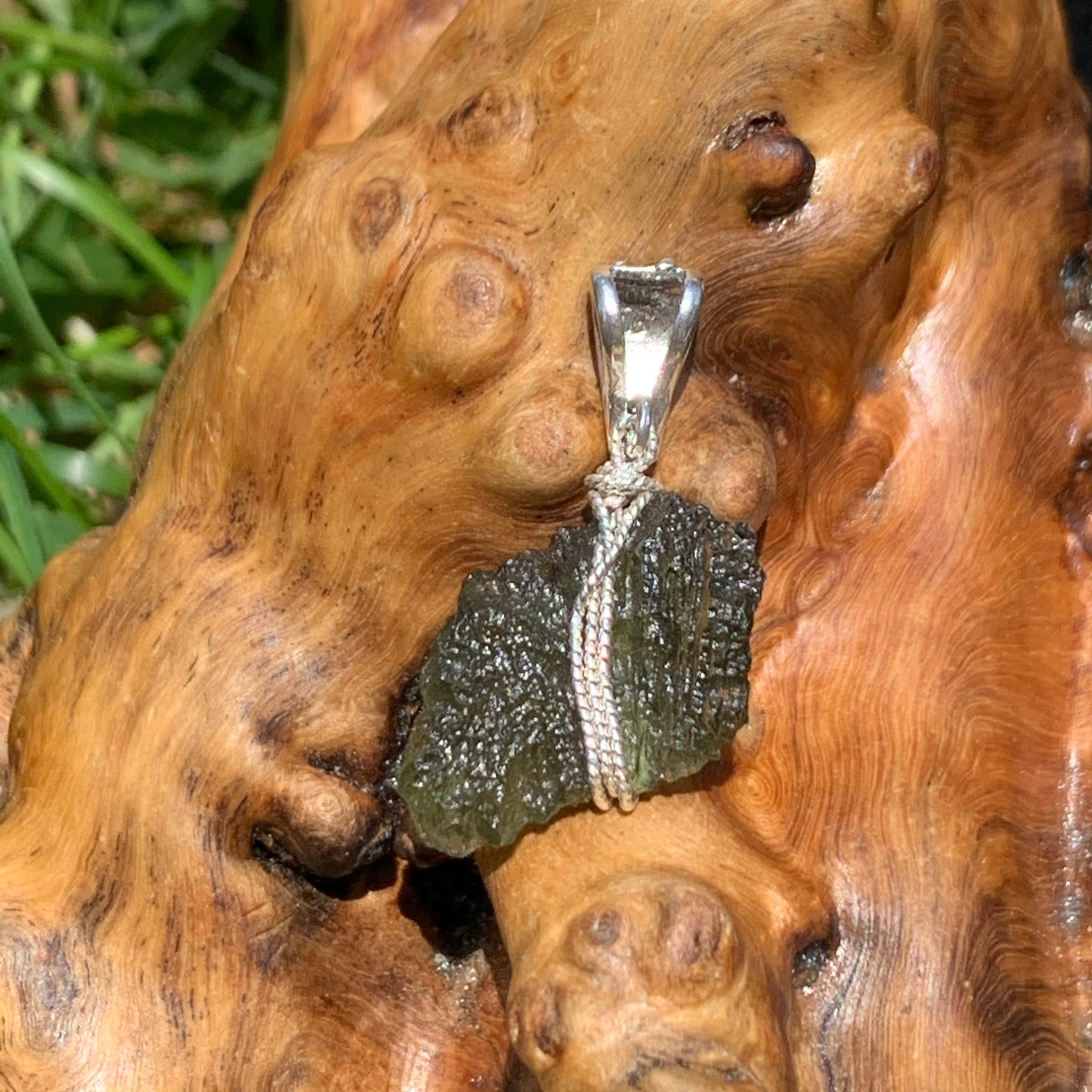 Moldavite pendant wire wrapped in sterling silver sitting on driftwood for display