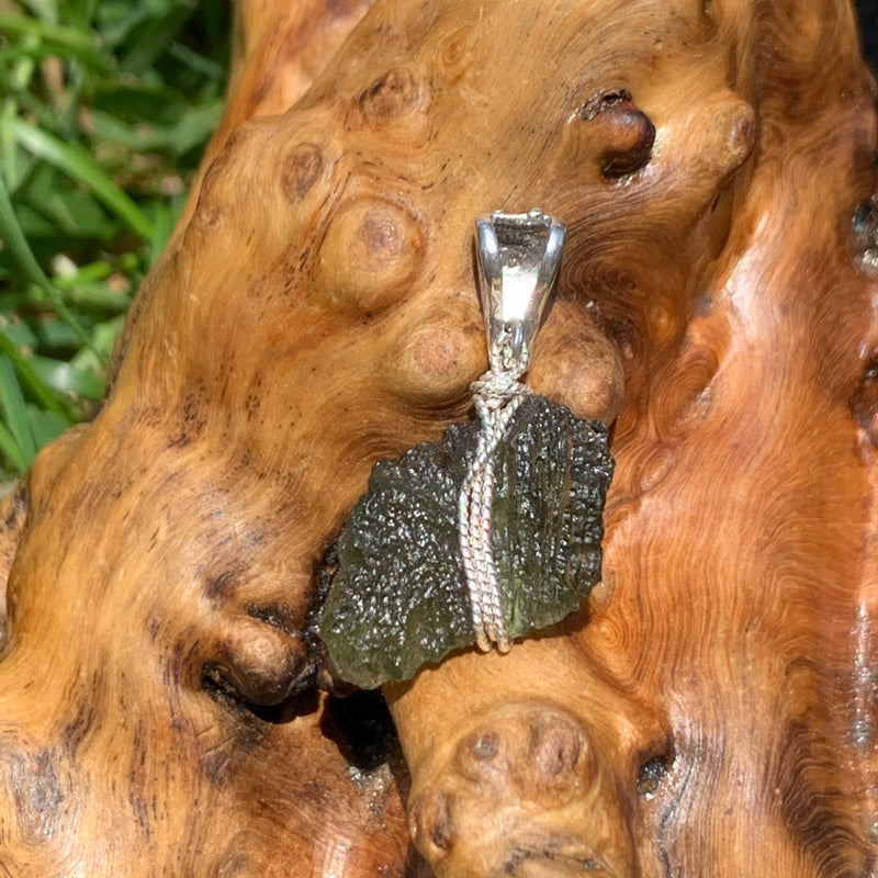 Moldavite pendant wire wrapped in sterling silver sitting on driftwood for display