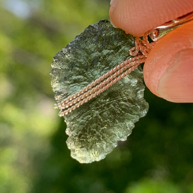 Moldavite pendant wire wrapped in sterling silver held with sunlight shining through