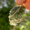 Moldavite pendant wire wrapped in sterling silver held with sunlight shining through