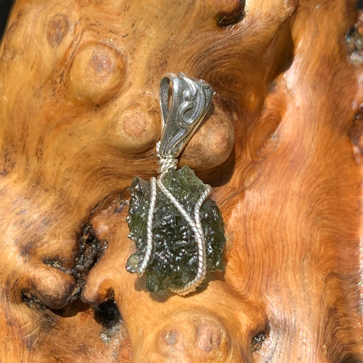 Moldavite pendant wire wrapped in sterling silver sitting on driftwood for display