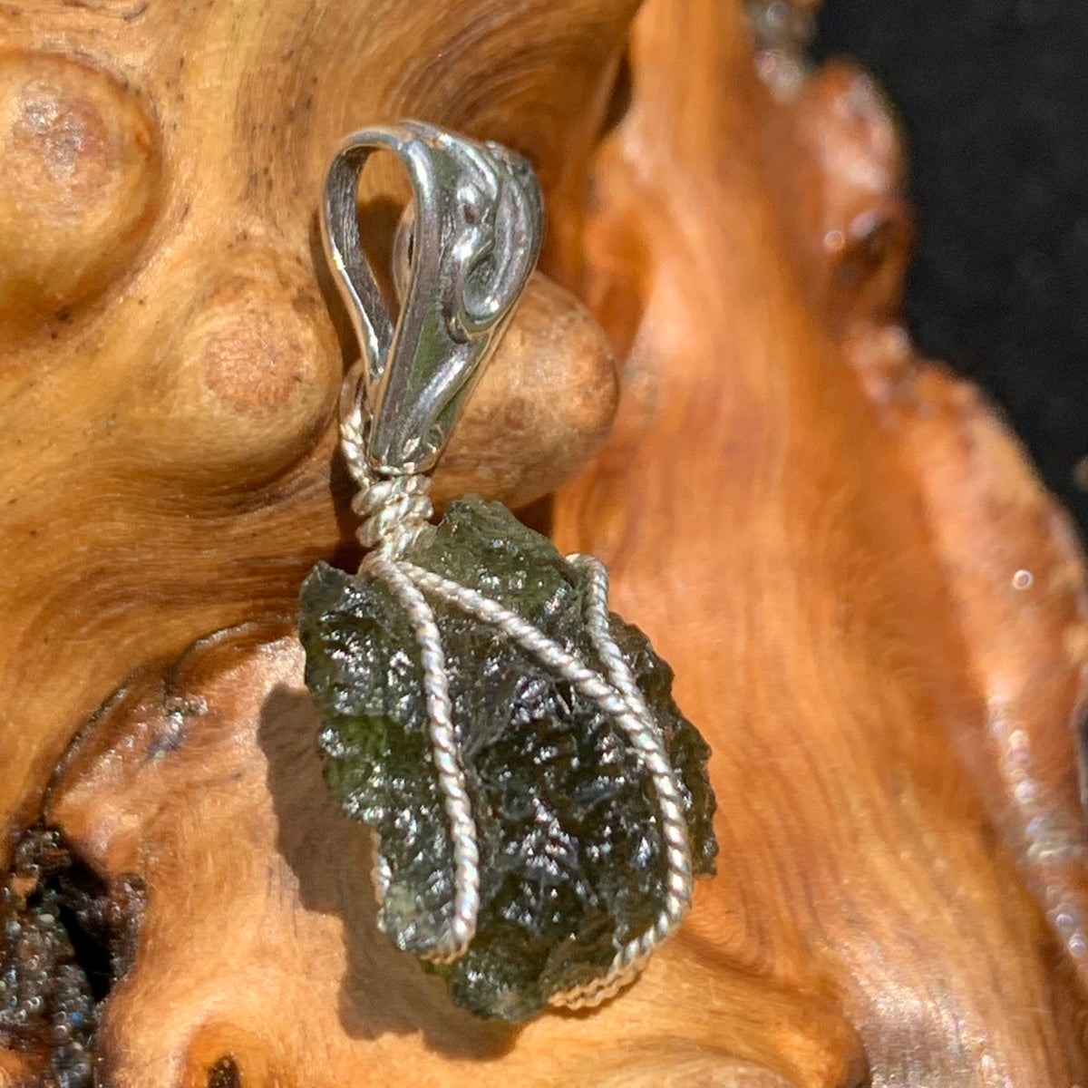 Moldavite pendant wire wrapped in sterling silver sitting on driftwood for display