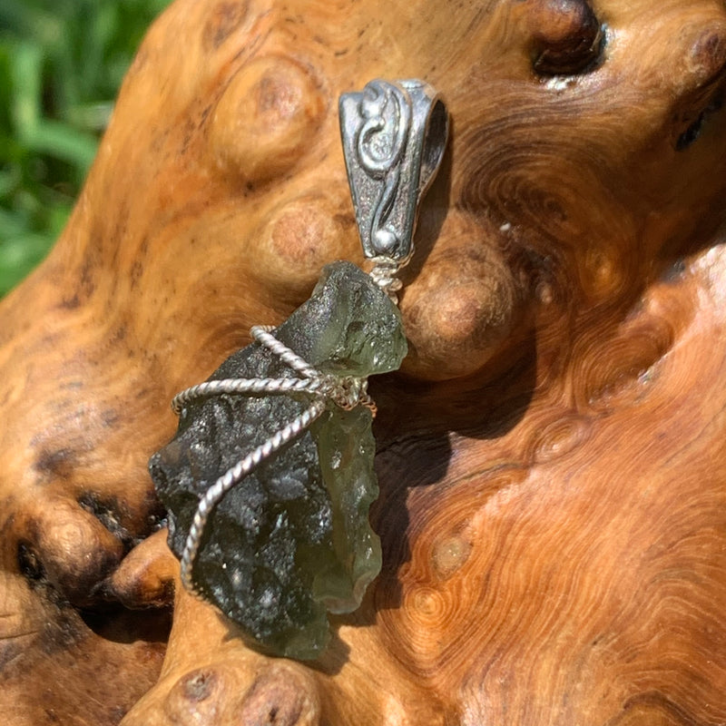 Moldavite pendant wire wrapped in sterling silver sitting on driftwood for display