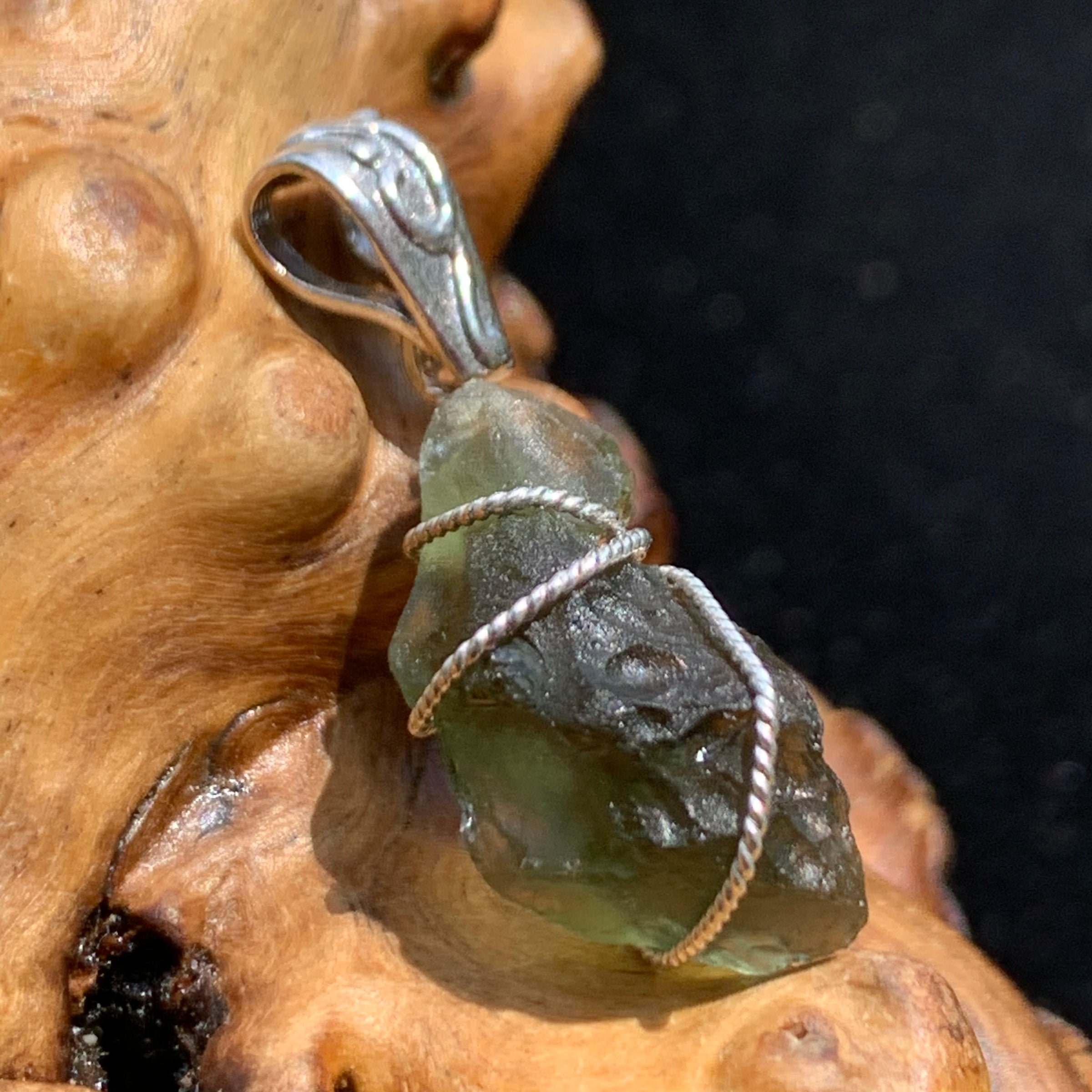 Moldavite pendant wire wrapped in sterling silver sitting on driftwood for display