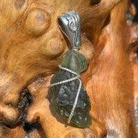 Moldavite pendant wire wrapped in sterling silver sitting on driftwood for display