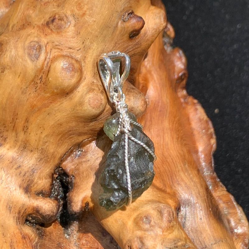 Moldavite pendant wire wrapped in sterling silver sitting on driftwood for display