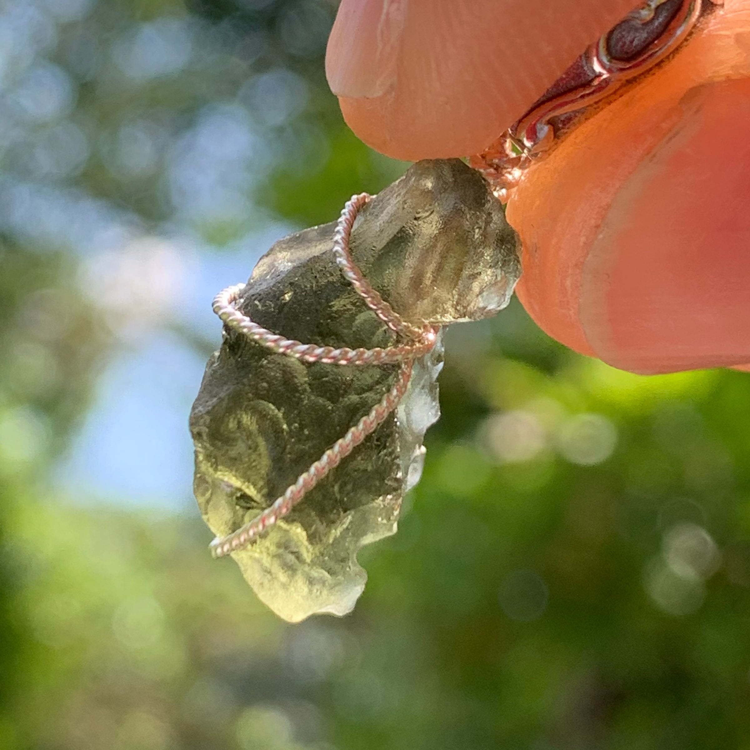 Moldavite pendant wire wrapped in sterling silver held with sunlight shining through