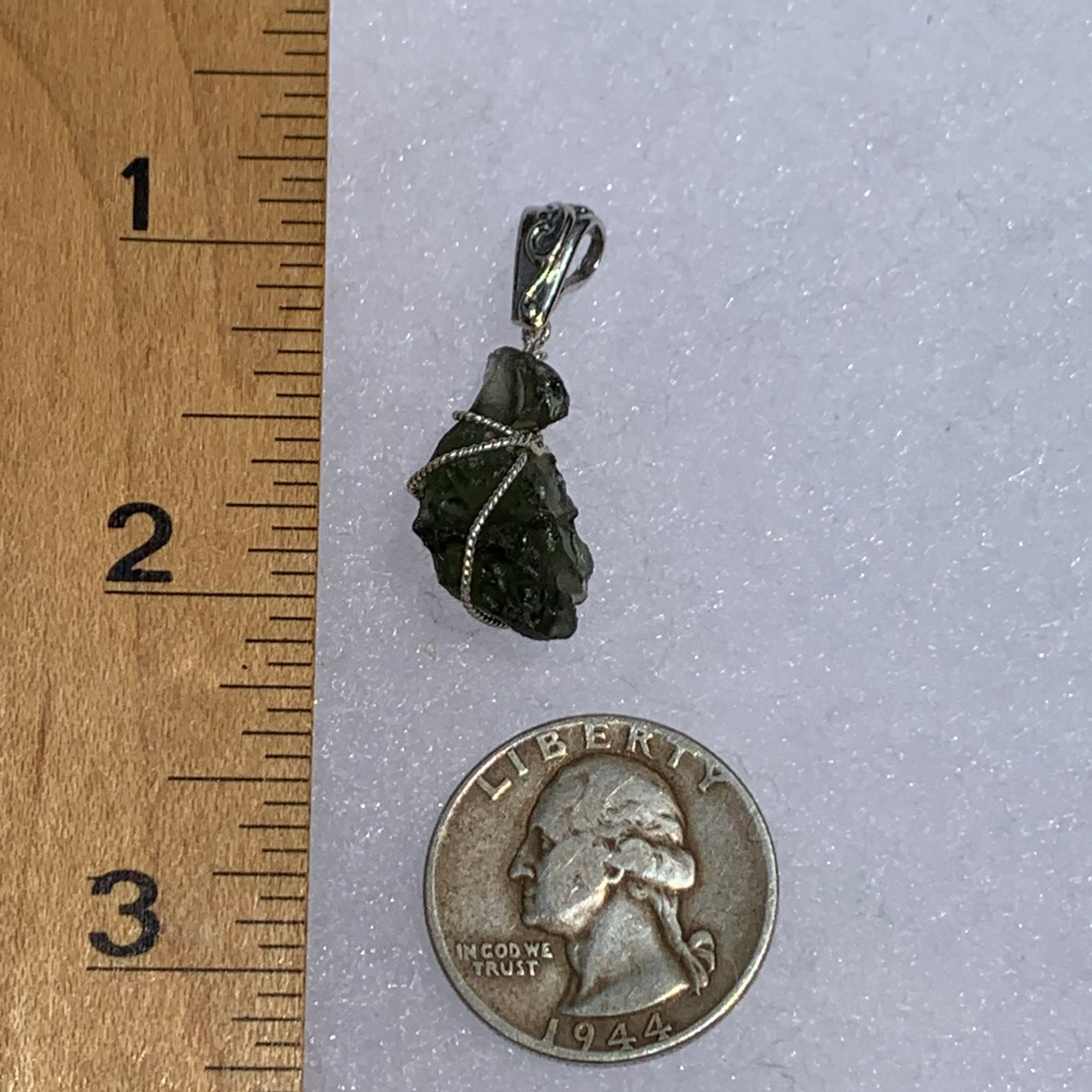 Wire wrapped moldavite pendant next to a ruler and US quarter to show scale