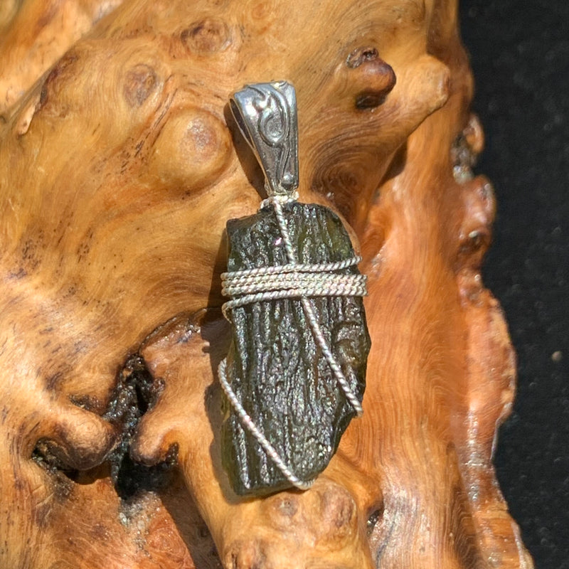 Moldavite pendant wire wrapped in sterling silver sitting on driftwood for display