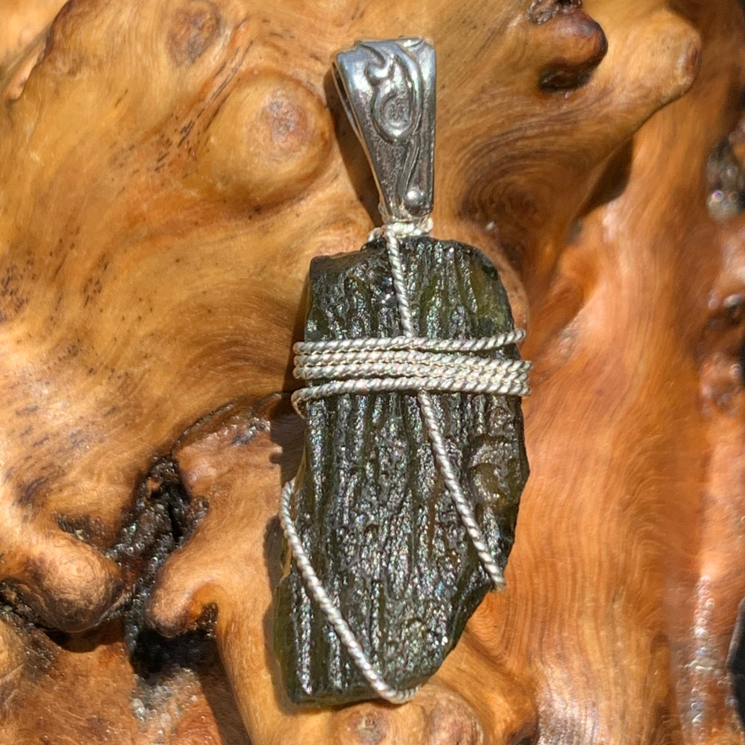 Moldavite pendant wire wrapped in sterling silver sitting on driftwood for display