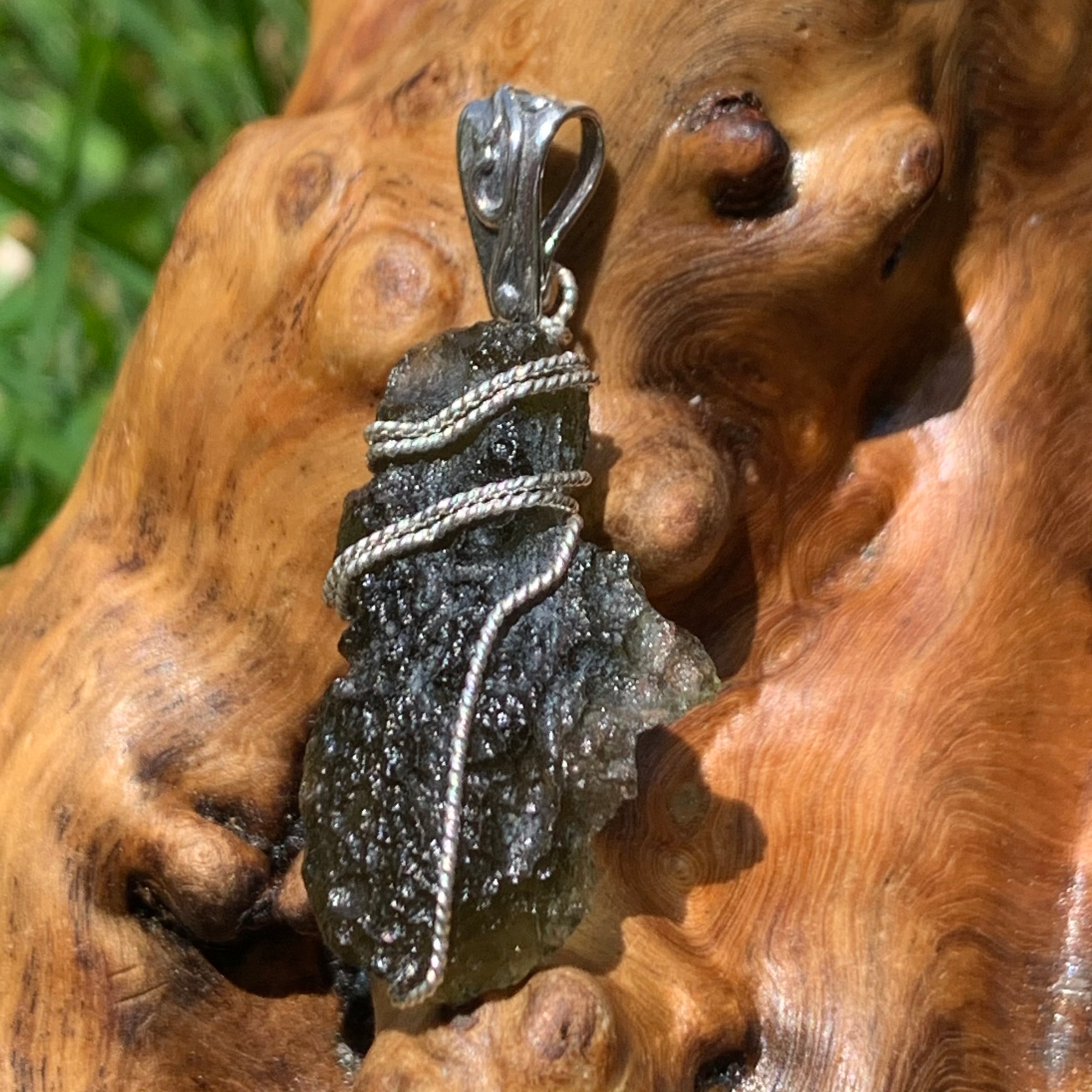 Moldavite sterling silver pendant displayed on driftwood