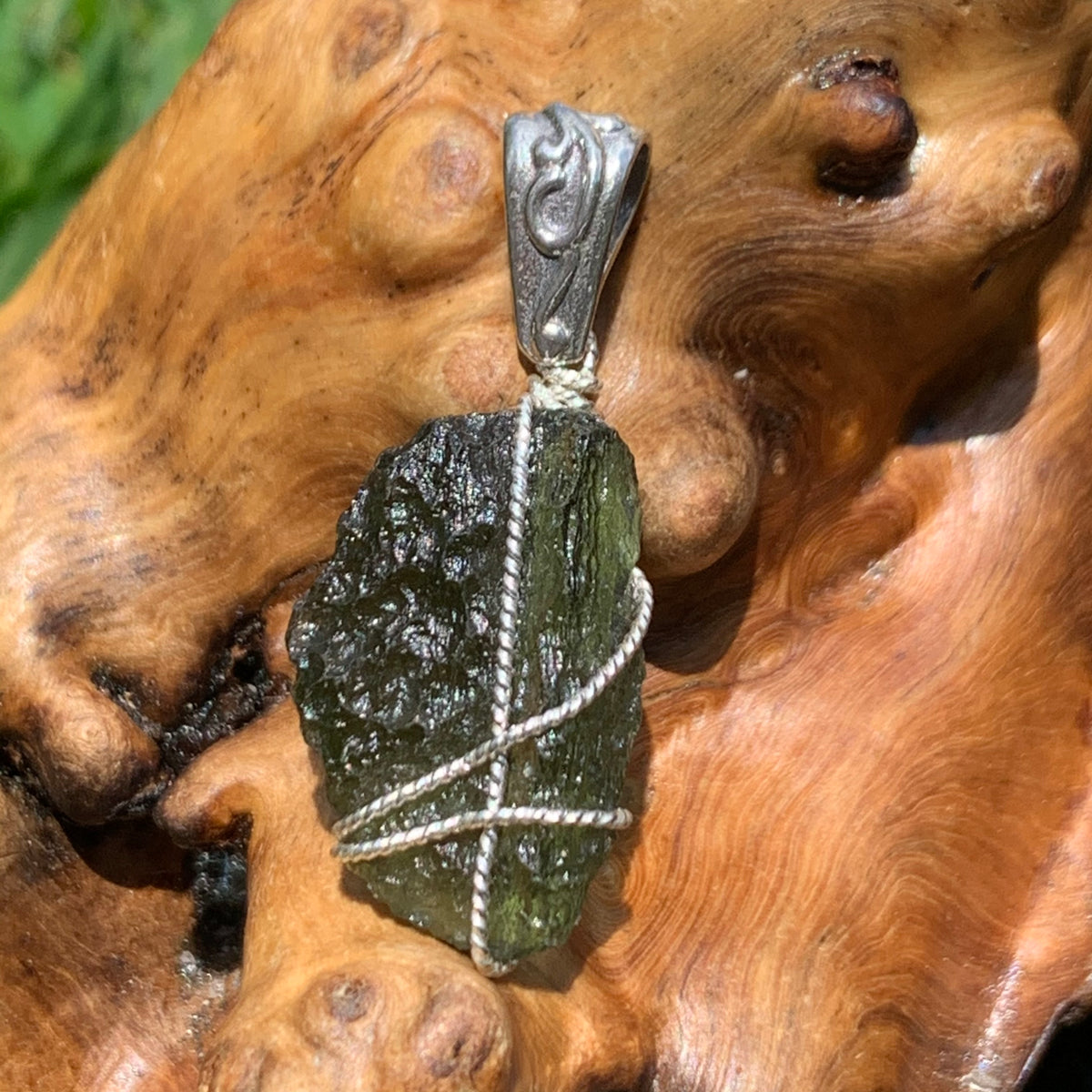 Moldavite sterling silver pendant displayed on driftwood