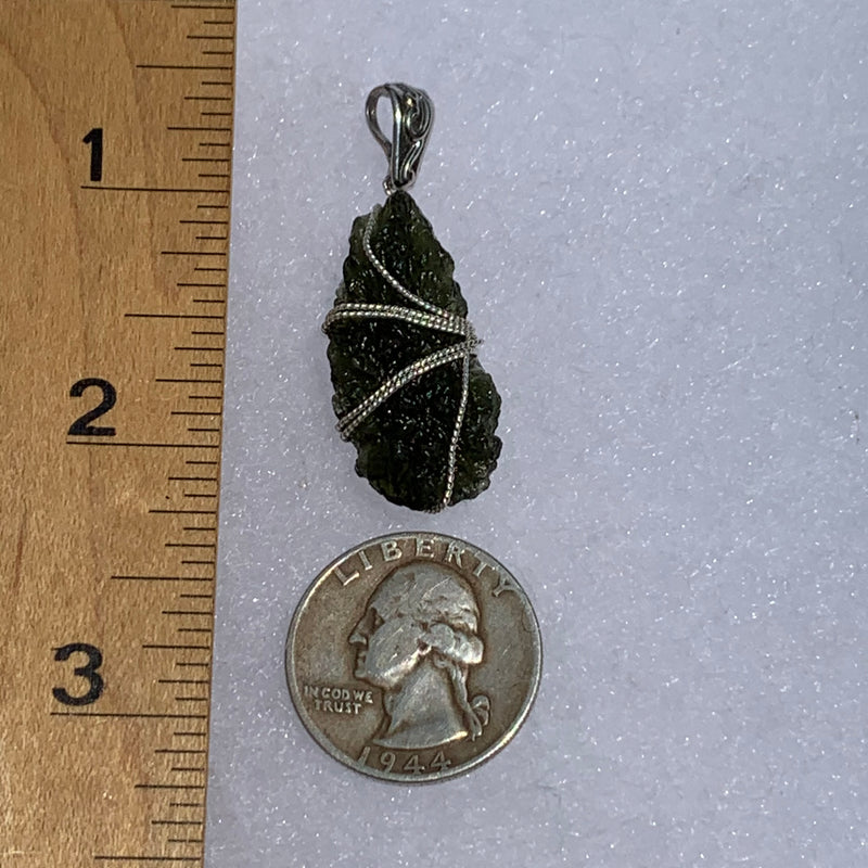 the silver moldavite pendant is next to a ruler and US quarter