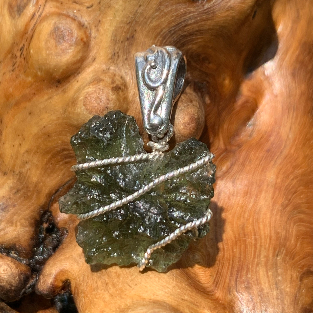 Moldavite sterling silver pendant displayed on driftwood