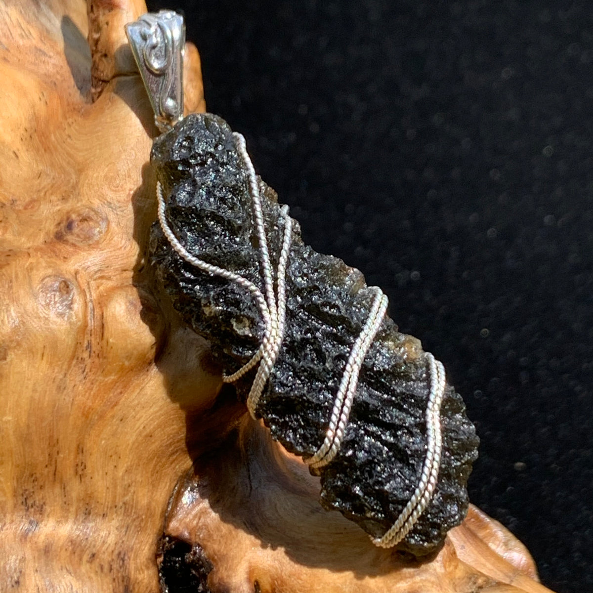 Moldavite sterling silver pendant displayed on driftwood