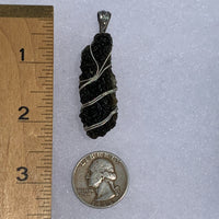 the silver moldavite pendant sits next to a ruler and US quarter