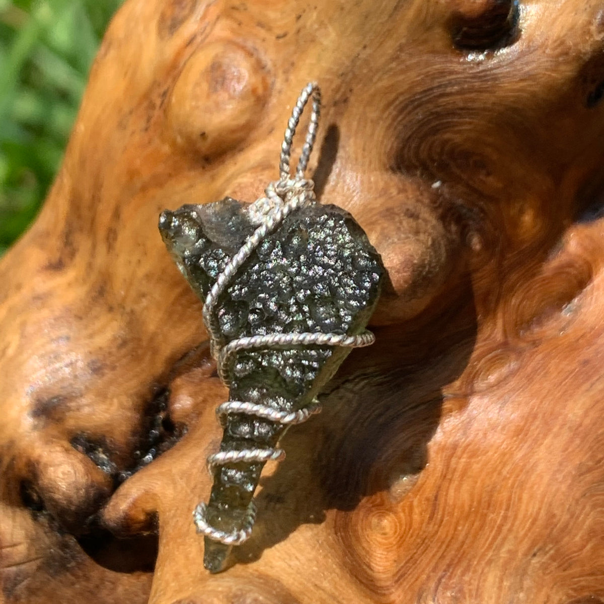 Moldavite sterling silver pendant displayed on driftwood