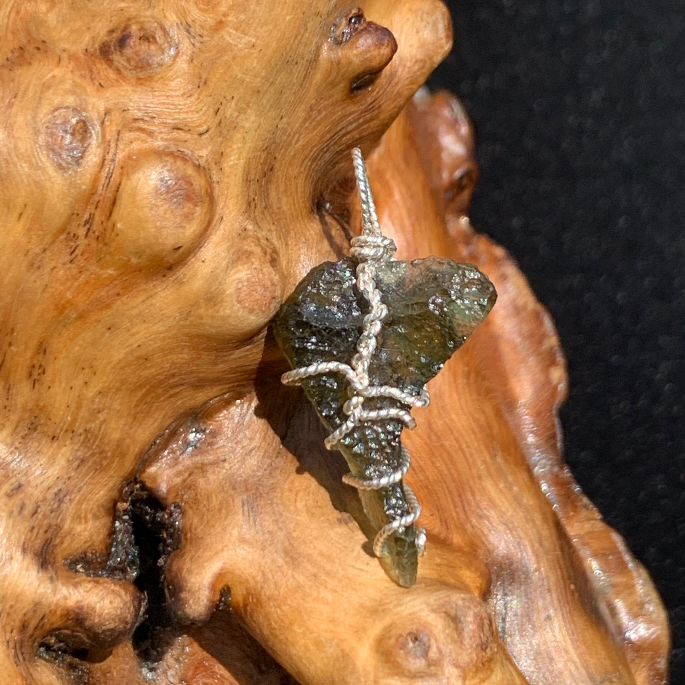 Moldavite sterling silver pendant displayed on driftwood