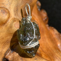 Moldavite sterling silver pendant displayed on driftwood