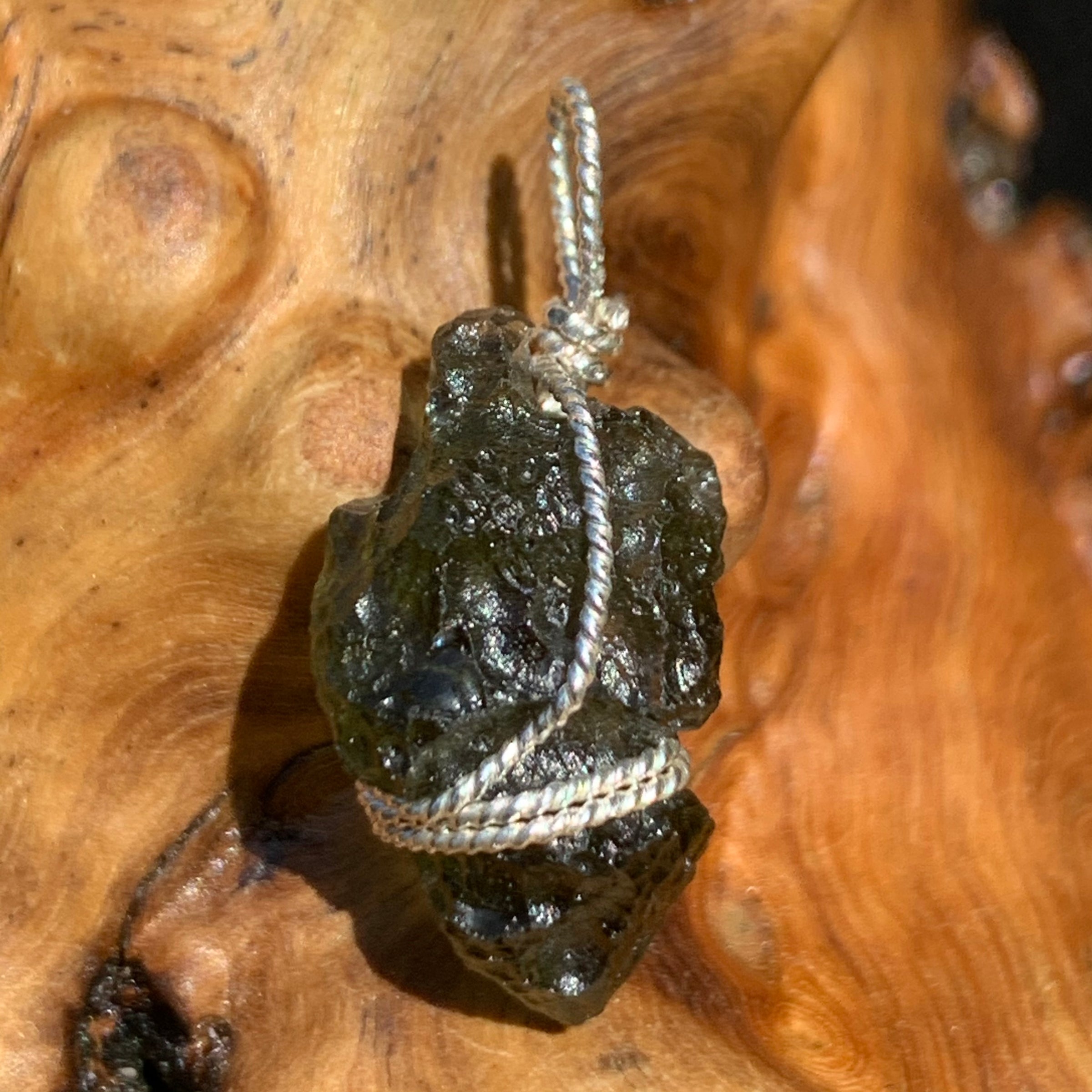 Moldavite sterling silver pendant displayed on driftwood