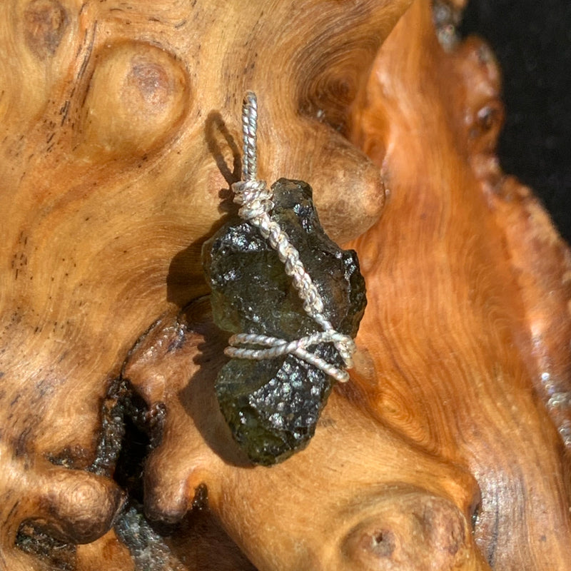 Moldavite sterling silver pendant displayed on driftwood