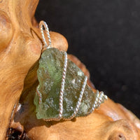 Moldavite sterling silver pendant displayed on driftwood