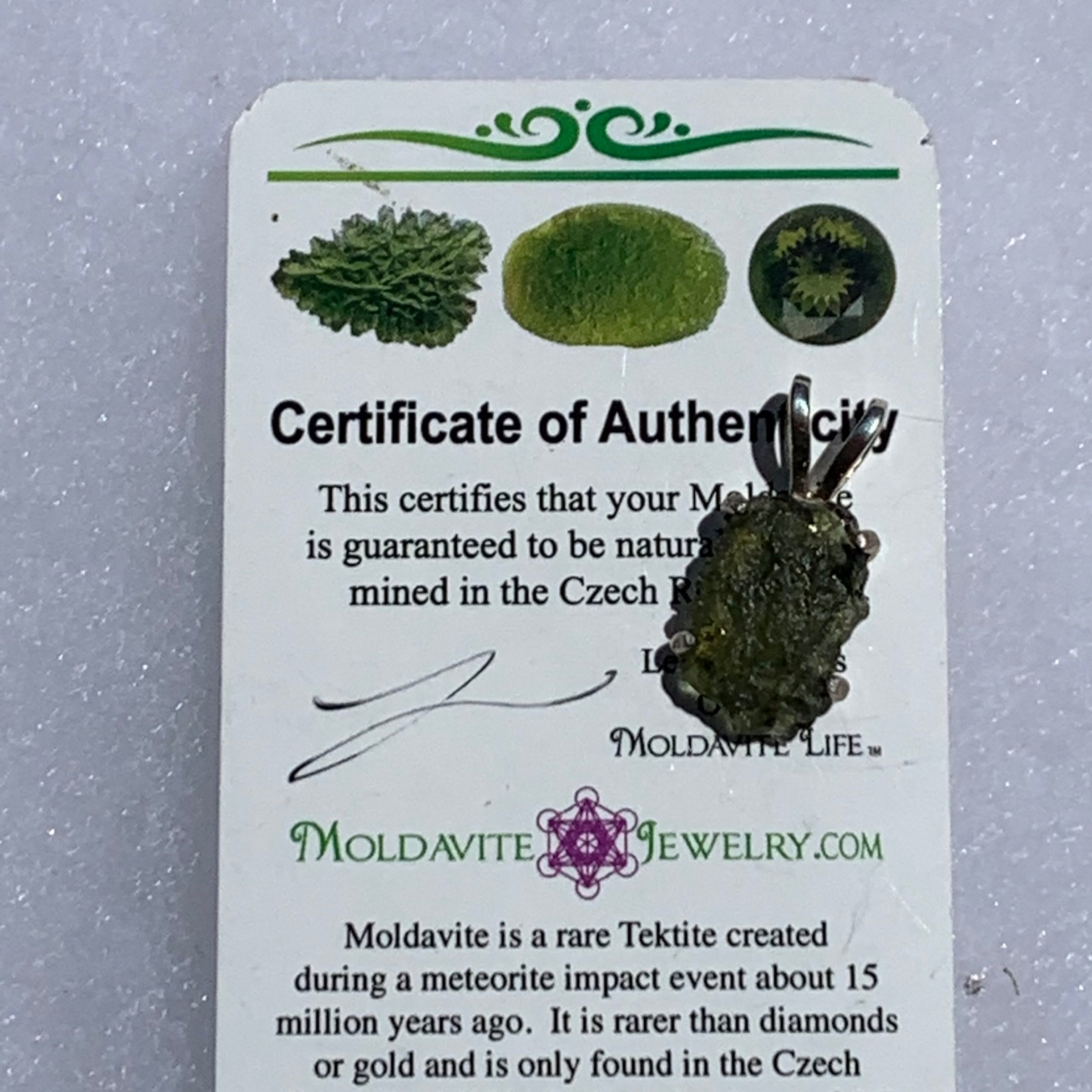 raw moldavite tektite in 4 prong sterling silver basket pendant sitting on moldavite certificate of authenticity for display