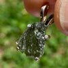 raw moldavite tektite in 4 prong sterling silver basket pendant held in hand with sunlight shining on it