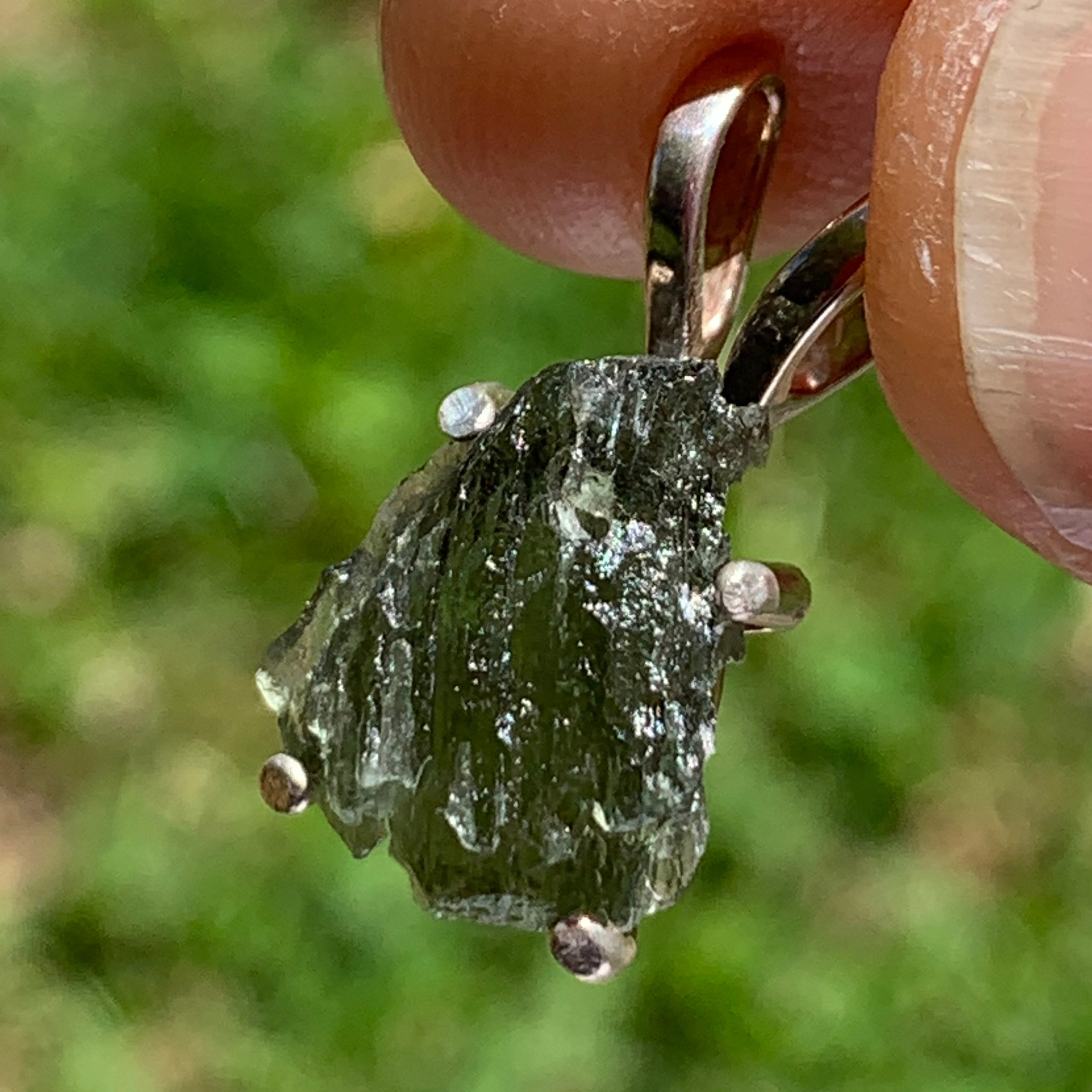 raw moldavite tektite in 4 prong sterling silver basket pendant held in hand with sunlight shining on it