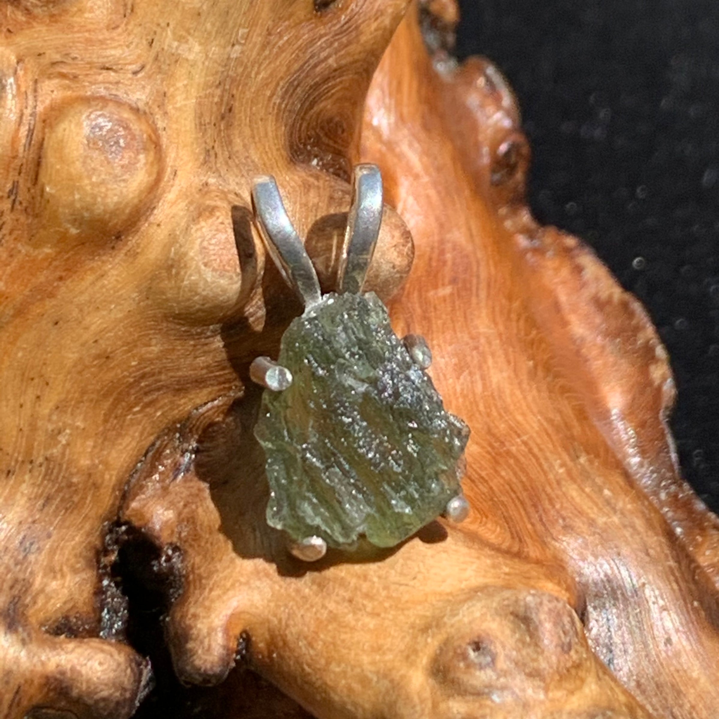 raw moldavite tektite in 4 prong sterling silver basket pendant sitting on driftwood for display