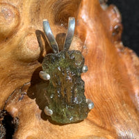 raw moldavite tektite in 4 prong sterling silver basket pendant sitting on driftwood for display