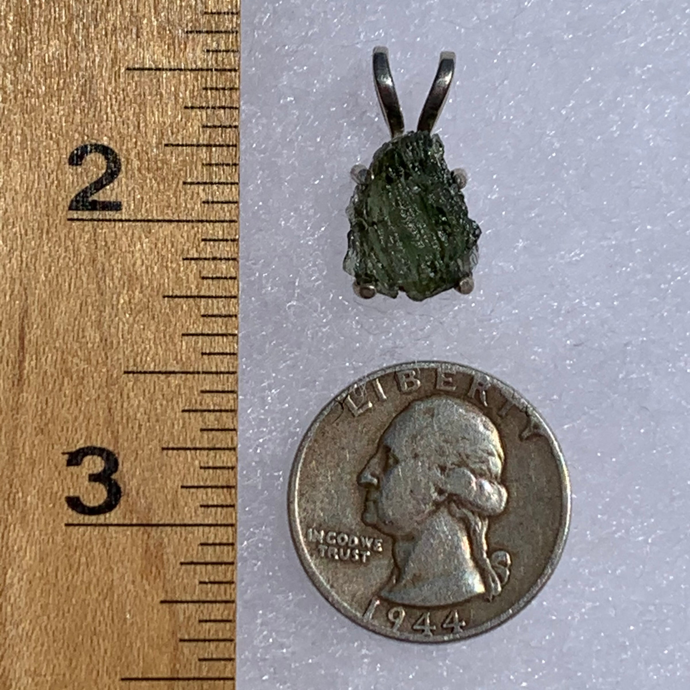 raw moldavite tektite in 4 prong sterling silver basket pendant next to a ruler and a quarter for scale