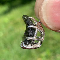 raw moldavite tektite sterling silver basket pendant held up on display to show details