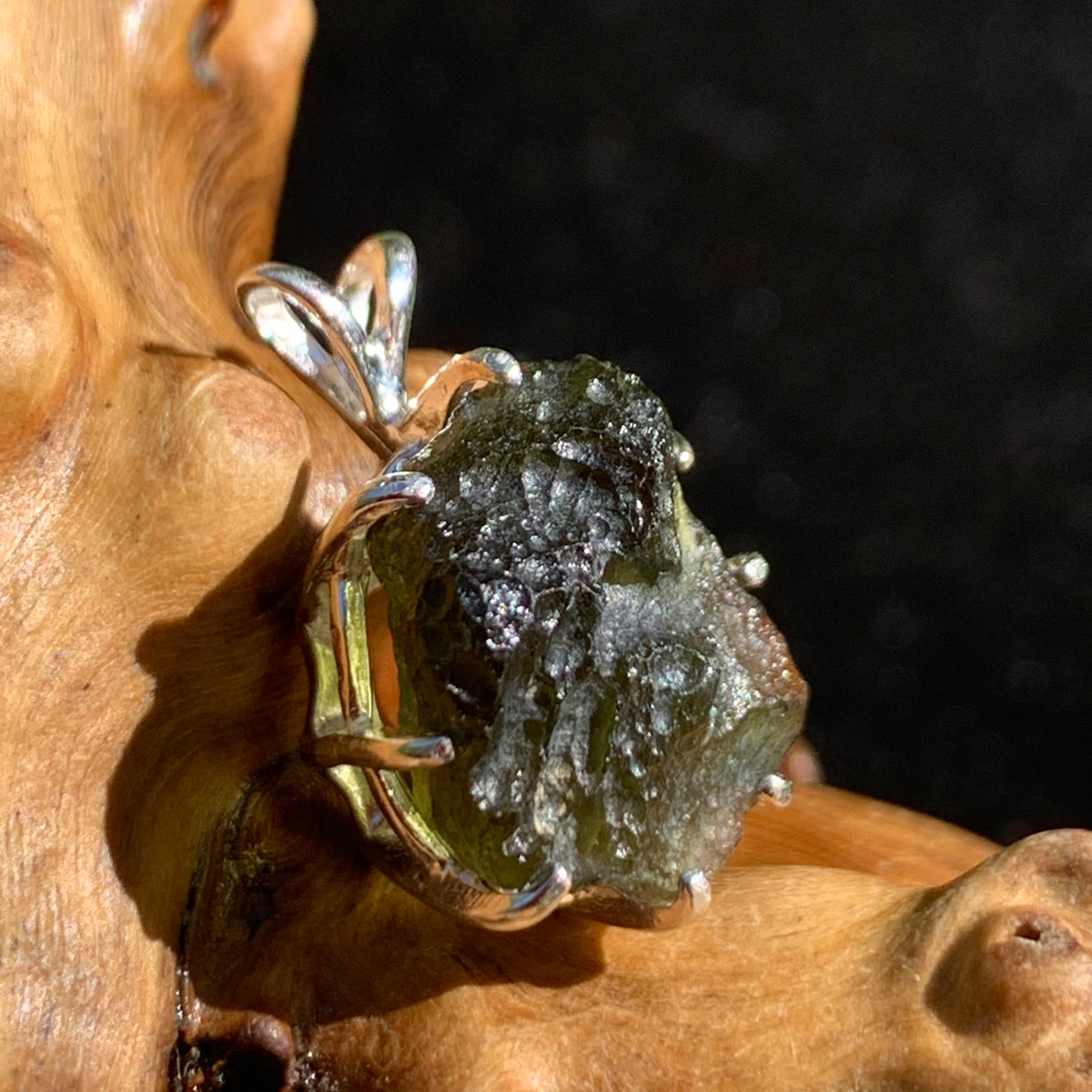 raw moldavite tektite sterling silver basket pendant sitting on driftwood for display