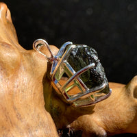 side view of a raw moldavite tektite sterling silver basket pendant sitting on driftwood for display