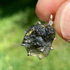 raw moldavite tektite sterling silver basket pendant held up on display to show details