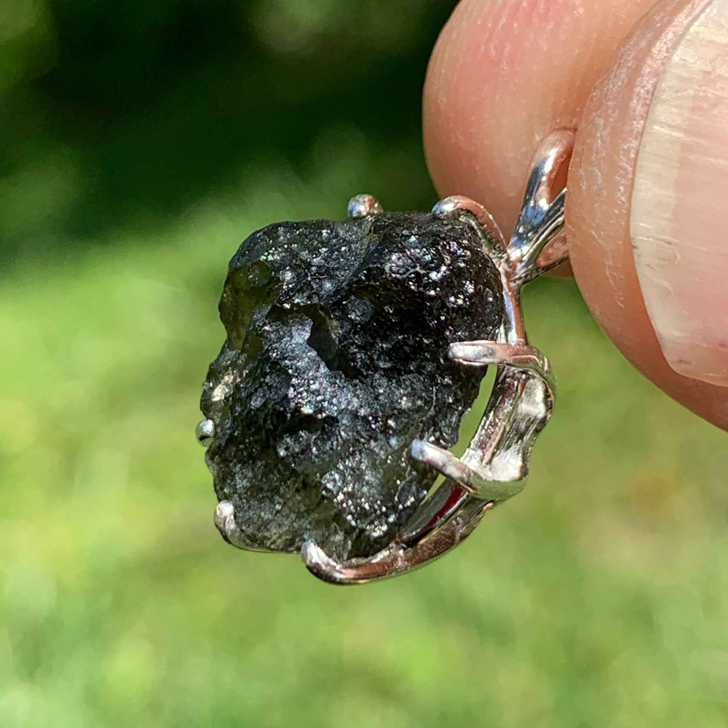 raw moldavite tektite sterling silver basket pendant held up on display to show details