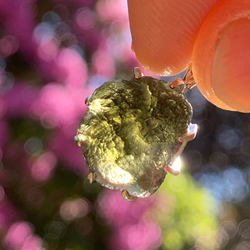 raw moldavite tektite sterling silver basket pendant held up on display with sunlight shining through to show details