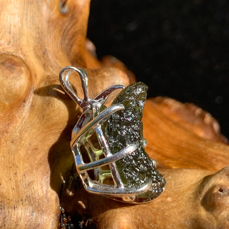 side view of a raw moldavite tektite sterling silver basket pendant sitting on driftwood for display