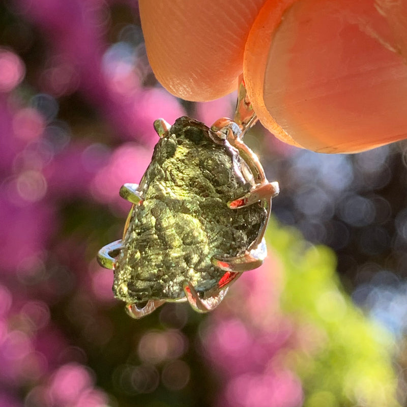 raw moldavite tektite sterling silver basket pendant held up on display with sunlight shining through to show details