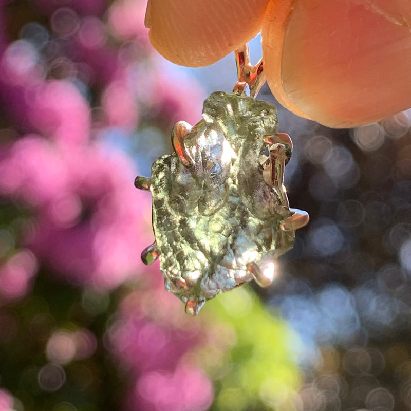 raw moldavite tektite sterling silver basket pendant held up on display with sunlight shining through to show details